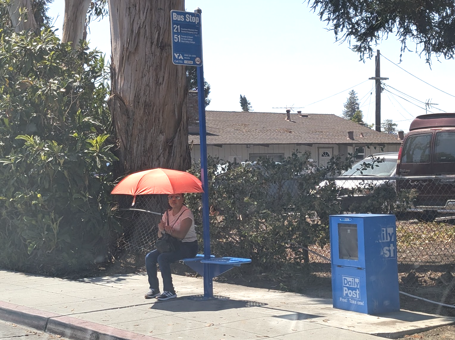 A person waiting for the bus under a personal umbrella for shade on Moffett Boulevard in Mountain View.